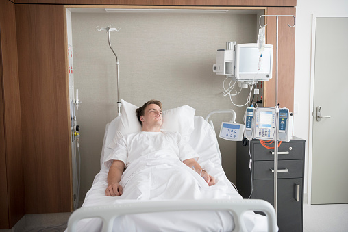 Young man lying in hospital with medical equipment and machinery next to the bed. Illness, health, recovery, rehabilitation.
