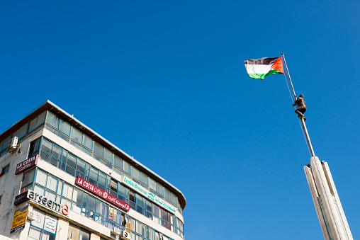 Ramallah, West Bank, Palestinian Territories - July 22, 2013: A clear blue sky is seen above the West Bank city of Ramallah. To the left is a building housing several businesses; to the right is a monument featuring the Palestinian flag.