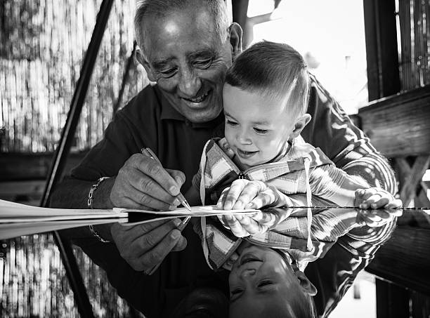 Grandfather and grandson having fun drawing something on paper on a glass table that reflects their faces.Black and white.