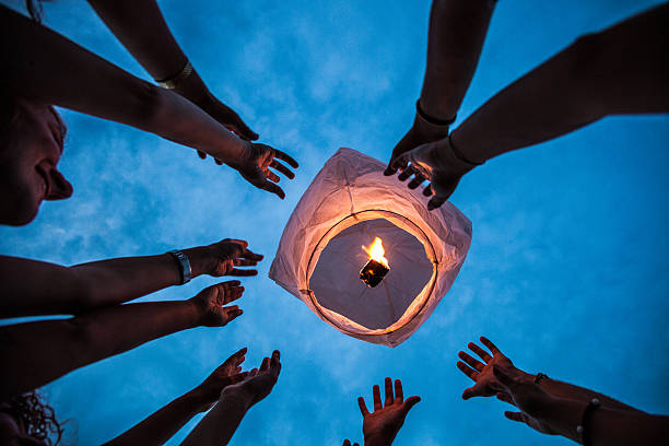 Lighting a paper lantern in the air Friends having a lot of fun at birthday party outdoor starting a Chinese lantern at the end of the event. chinese lantern stock pictures, royalty-free photos & images