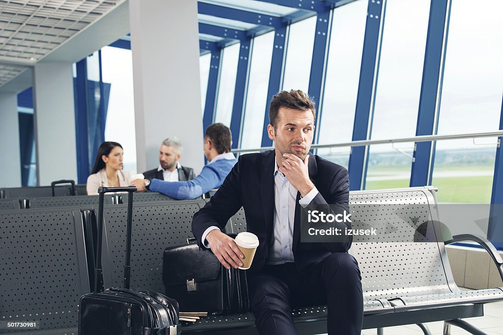 At the airport Businessman waiting for a flight at the airport lounge, sitting bored on a banch, group of people in the background. Airplane Stock Photo