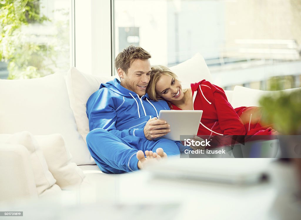 Young couple using a digital tablet Young couple lying down on sofa in their apartment and using a digital tablet together.  Couple - Relationship Stock Photo