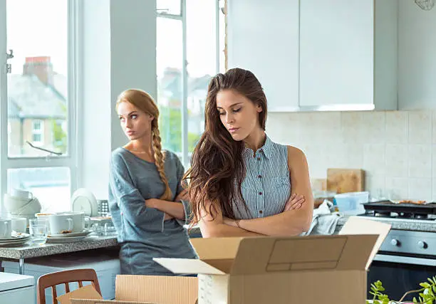 Two girls having quarrel at home, giving up the cohabitation. Cardboard boxes on the table.