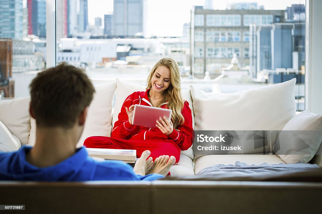 Young couple in an apartment Focus on the young man sitting on sofa in an apartment and using a digital tablet. 20-24 Years Stock Photo