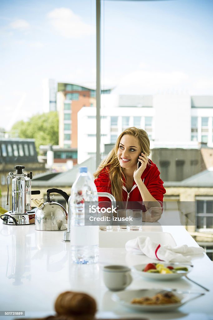 Young woman in an apartment Young woman standing in front of window in the kitchen in her apartment and talking on phone. 20-24 Years Stock Photo