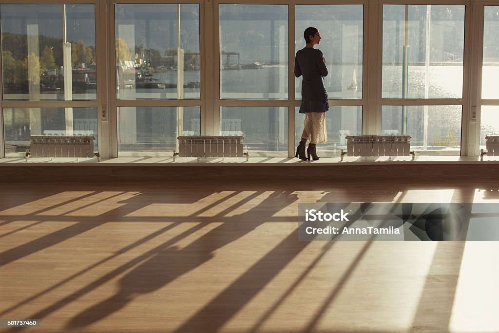 Woman standing near large window and looking to sunset Woman standing near large window and looking to sunset. Big window, glass wall, warm room, sun and sea 2015 Stock Photo