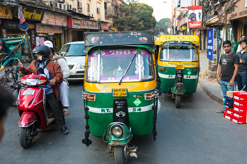 Calcutta, India - January 4, 2014: Urban street, ickshaws, tuk-tuk in green and yellow color and motorbike side by side on urban street in residental district. Some people on the pavement. 