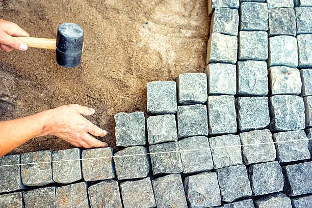 Photo of industrial worker installing pavement rocks, cobblestone blocks on road pavement