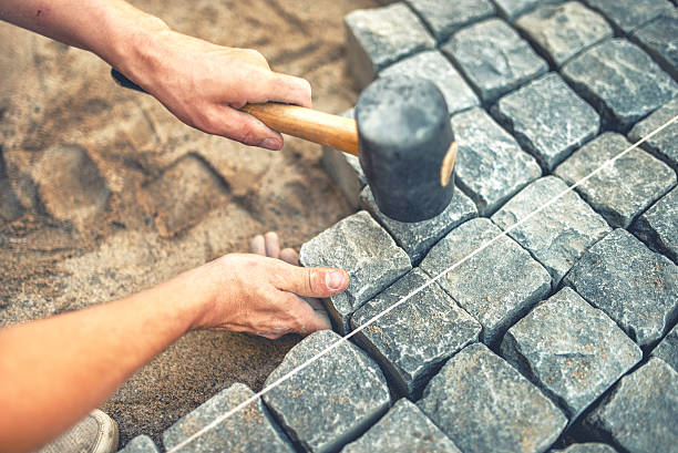 istock worker using stones and rubber hammer to build stone sidewalk 501748660