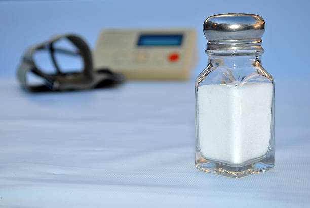 Health, Salt, Blood Pressure A salt shaker with a blood pressure gauge in the background. Healthy diet for a healthy heart. 120/80. sodium intake stock pictures, royalty-free photos & images