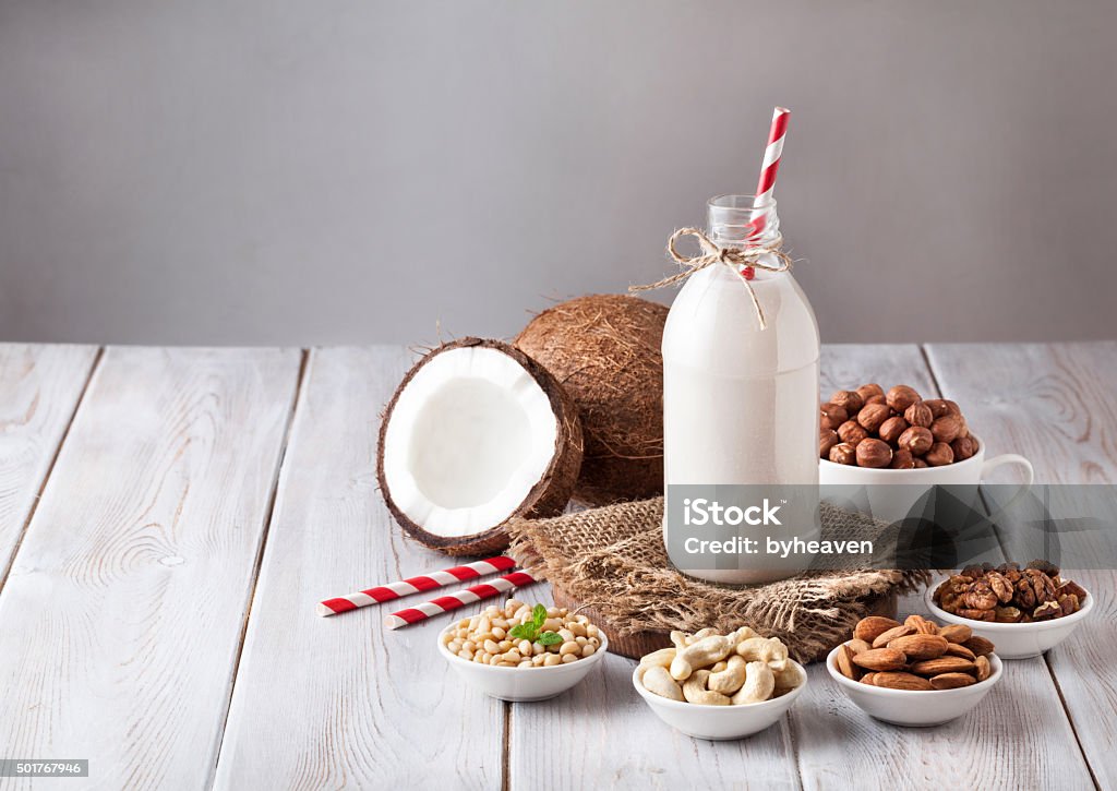Vegan nut milk in the bottle Vegan milk from nuts in the bottle with red stripped straw around various nuts on white wooden table Vegetable Stock Photo