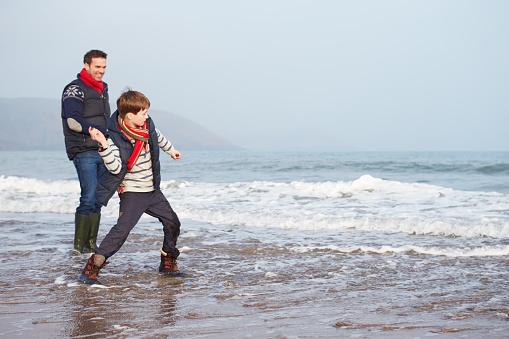 Father And Son Walking On Winter Beach And Throwing Stones