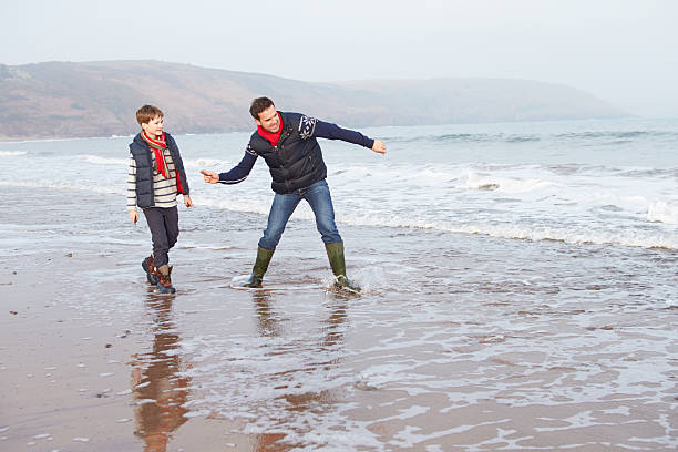 padre e figlio a piedi sulla spiaggia e lanciando pietre inverno - throwing people stone tossing foto e immagini stock