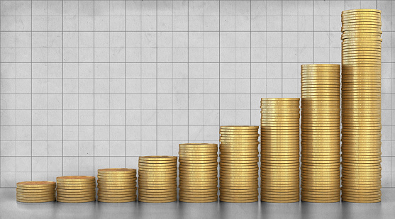 Stacks of gold coins arranged in front of a rugged paper background with vertical and horizontal lines. The stacks height is rising from left to right in an exponential fashion, imitating a graph curve.