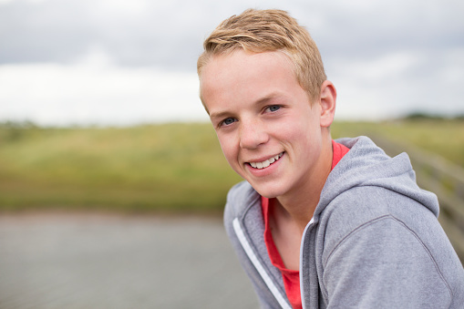 Portrait of a teenage boy smiling at the camera. He is outdoors and wearing casual clothing.