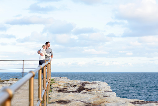 Couple on vacation looking at view from jetty on rocks. Two people on holiday  with arms around each other.