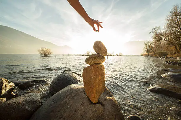 Detail of person stacking rocks by the lake. Sunset time, sunbeam.