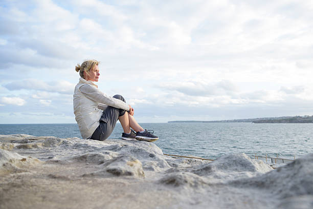 istock Mature woman sitting alone on rocks, looking at view 501794112