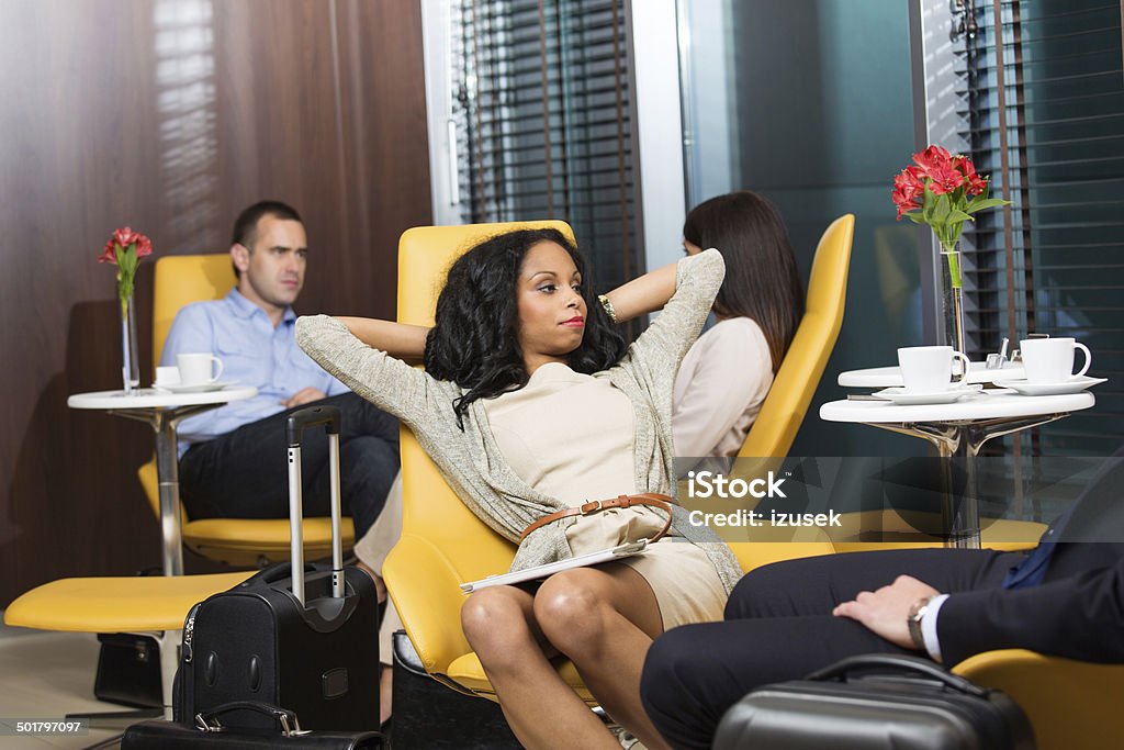 Business people waiting for the flight Business people waiting for a flight at the airport vip lounge. Focus on businesswoman sitting comfortably in armchair and stretching her arms. Airport Departure Area Stock Photo