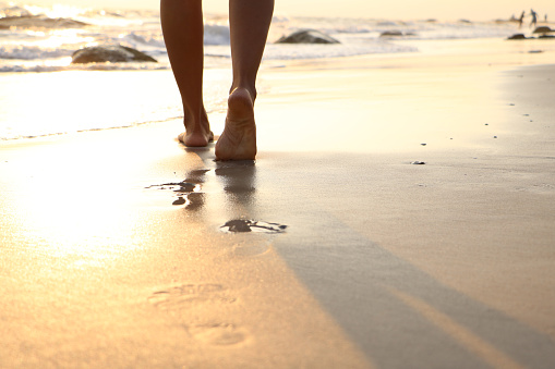 Girl walking on wet sandy beach leaving footprints in the sand at sunset time