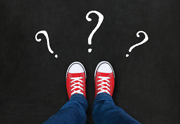 istock Feet wearing red shoes on black background with question marks. 501812378