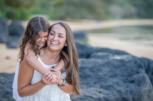 A mother and daughter are hugging on the beach on mother's day. They are enjoying their vacation in Hawaii together.