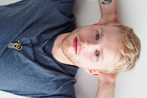 Close up portrait of the facial features of a Latino albino man. His long white lashes shield his blue eyes from the sunlight. He wears all-white clothing and poses against a white background. monochrome.