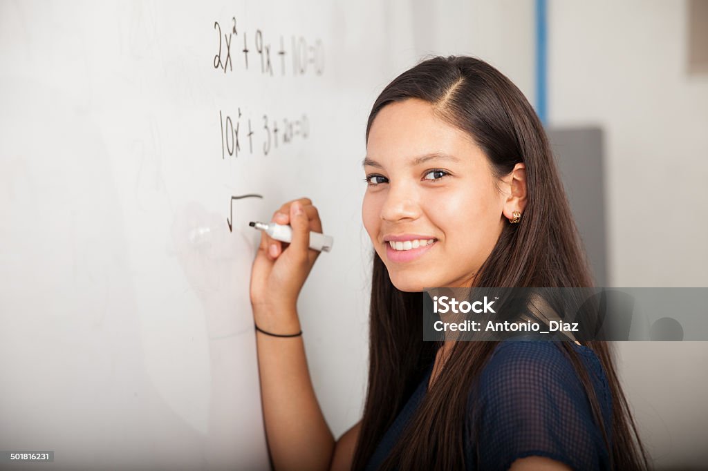 Happy math student in class Beautiful Hispanic student writing on a white board at school and smiling Mathematics Stock Photo