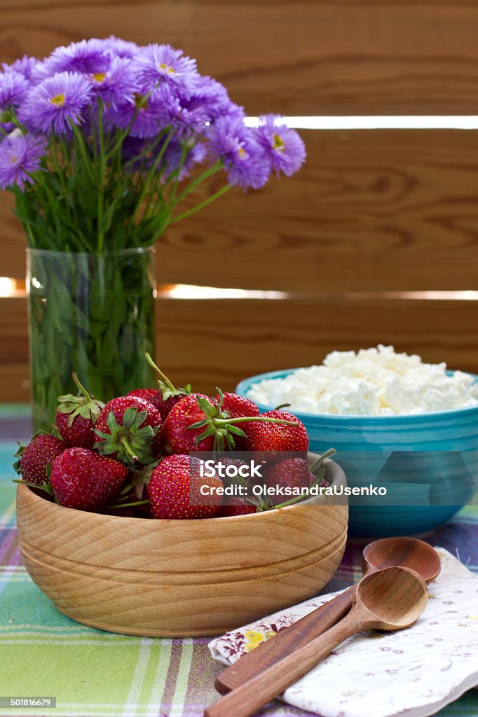 Strawberries in the wooden bowl and cottage cheese Strawberries in the wooden bowl, cottage cheese and violet flowers on the table Berry Fruit Stock Photo