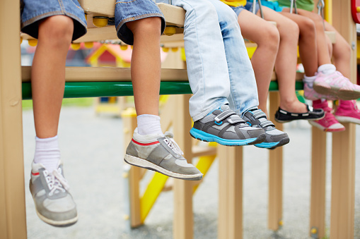Legs of little friends sitting on swing or other recreational facility