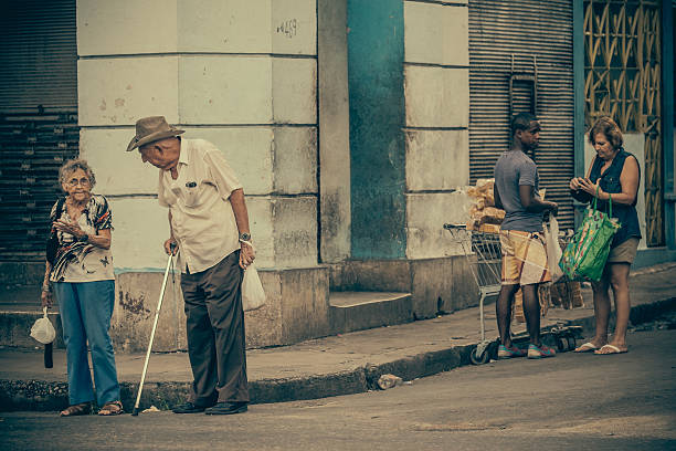 Havana, Cuba-November 7, 2015. Busy residential street of Centro Havana. Old man talking to old woman before crossing the road. Man in the background selling groceries out of his shopping car to older lady. Old, rundown residential buildings, remembering better times from 50 years ago. Street life in full effect: lot of people on the street. Facades are in bad shape due to long time neglect and poverty.