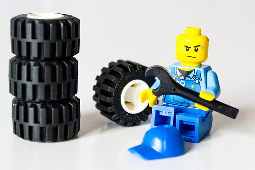 Florence, Italy - December 17, 2015: Lego minifigure mechanic is wearing a blue cup and sit in fronto of wheels