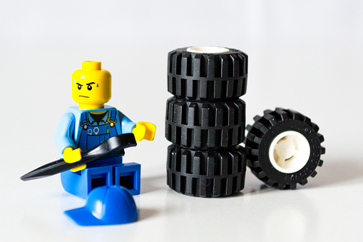 Florence, Italy - December 17, 2015: Lego minifigure mechanic is wearing a blue cup and sit in fronto of wheels