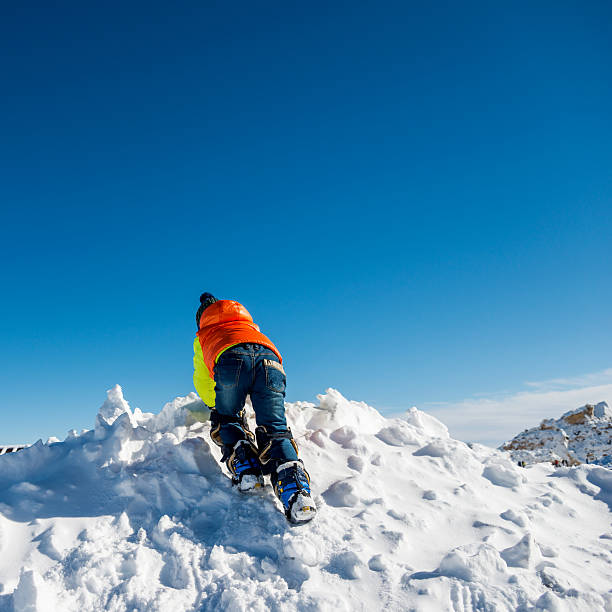 Two mountaineers in red high-altitude expedition gear carefully navigate a snowy crevasse secured by rope under harsh weather conditions with blowing snow.