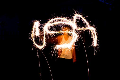 Young woman writing USA in light with a sparkler firework.