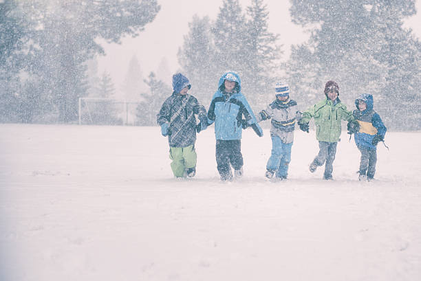 A group of 5 children run in a snowy storm at recess in a field at school