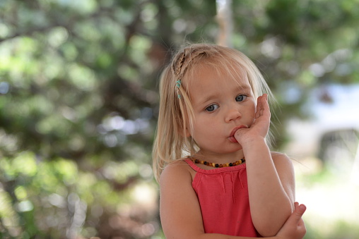Close up of a toddler girl sucking her thumb using a lot of body language to express herself.