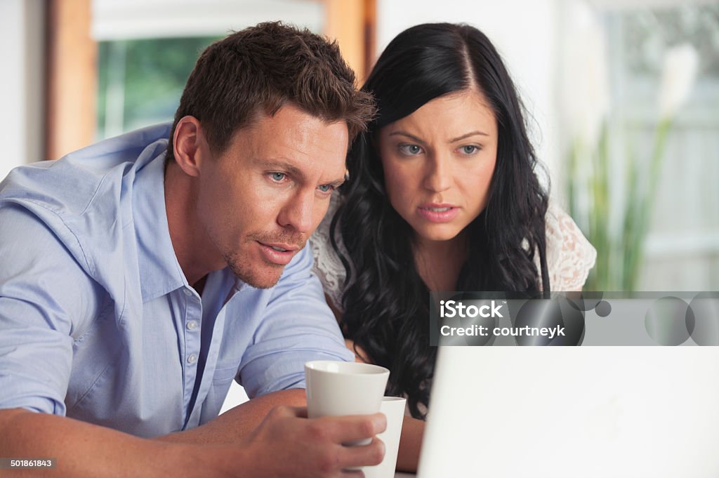 Worried Couple looking at laptop computer Worried Couple looking at laptop computer drinking coffee 20-24 Years Stock Photo