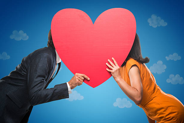 Quirky Stylish Couple Kissing Quirky stylish couple hiding behind a big red heart. blind date stock pictures, royalty-free photos & images