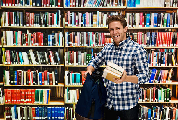 istock Smiling male student holding books in library 501887734