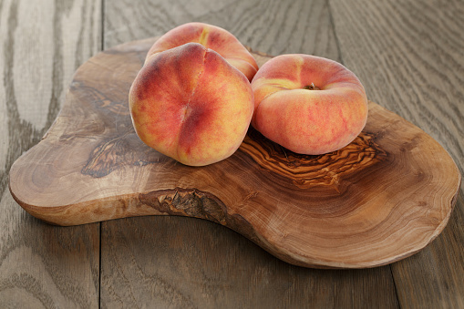 ripe flat peaches on olive board, rustic style