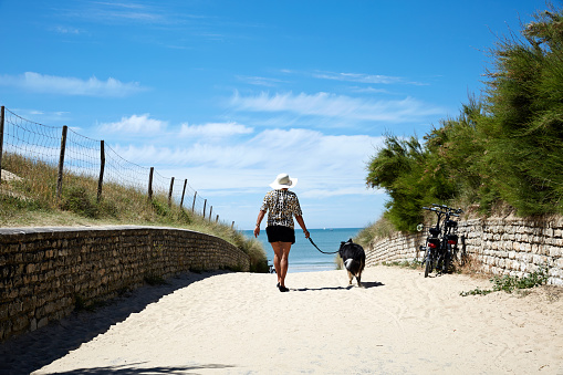 Mature smiling hispanic woman with dog walking on beach path