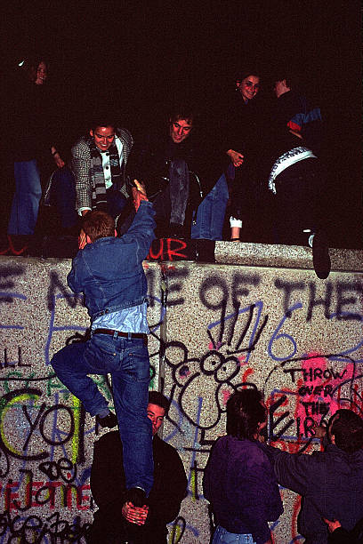 Fall of the Berliner wall November 1989 Berlin, germany - November 9, 1989:  "These is a scanned film" Fall of the Berliner wall November : The night of the of the fall of the wall in Berlin. People from West Berlin are climbing on the wall at the Pariser Platz, where the Brandenburger Gate is located. In these picture people are helping each other to climb on the wall. These picture is taken from the West Side, you can recognize it as there are Grafittis on the wall. The wall from the east side is only white. A very historivcal momemt. Two days ago these image woud not have been possible, the nnational police force of the German Democratic Republic had the order to kill anybody trying to cross the boarder. "These is a scanned film" east berlin photos stock pictures, royalty-free photos & images