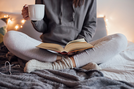 Chica bebiendo té caliente y libro de lectura en la cama photo