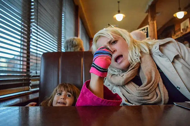 Little girl puts her socked foot on the table at a restaurant, her mother looks on in horror