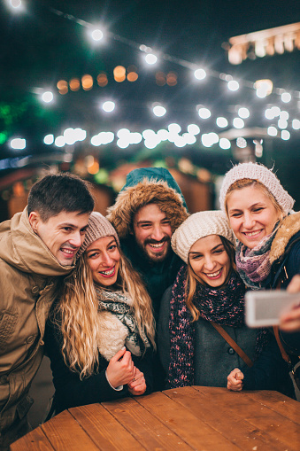 Couple of friends spending some time together on a Christmas market on a cold December day and making a selfie to remember precious Christmas moments 