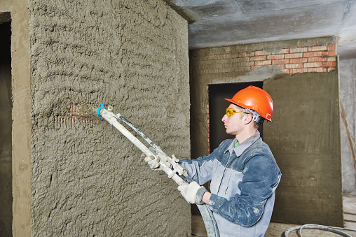 Plasterer operating sprayer equipment machine for spraying thin-layer putty plaster finishing on brick wall 