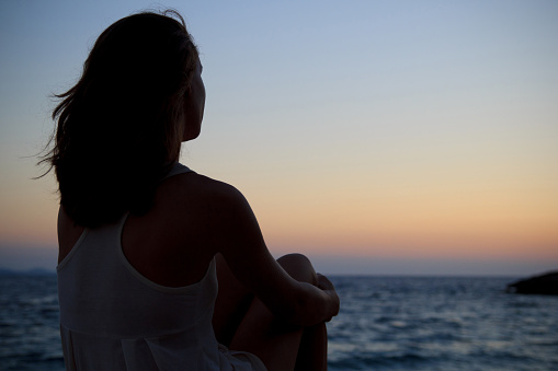 Lonely young woman, watching the sea sunset