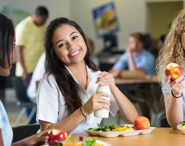 Photo of Cute Hispanic teenager having lunch with friends in school cafeteria