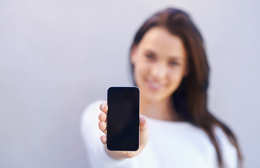 Portrait of an attractive young woman standing against a gray background and holding up her mobile phonehttp://195.154.178.81/DATA/i_collage/pi/shoots/783719.jpg
